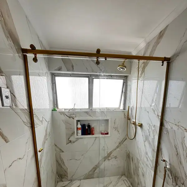 Box de correr com perfil dourado em banheiro de mármore calacata, obra da PS do Vidro